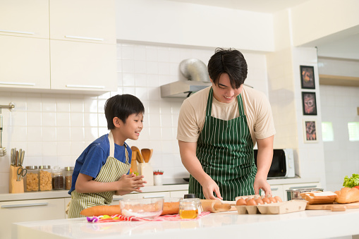 Happy Young Asian father and son cooking in kitchen at home