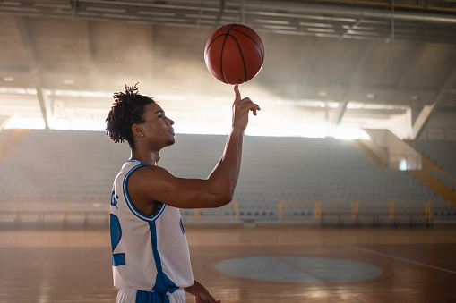 Young black athlete balancing leather basketball on finger.