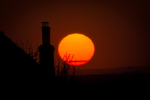 A beautiful bright orange English spring sun set with a silhouette of a chimney and tv aerial in the the foreground