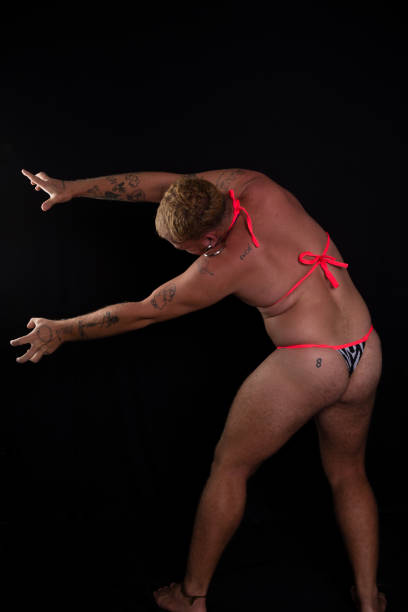 Young, handsome man wearing bikini and making body gestures. isolated on dark background.