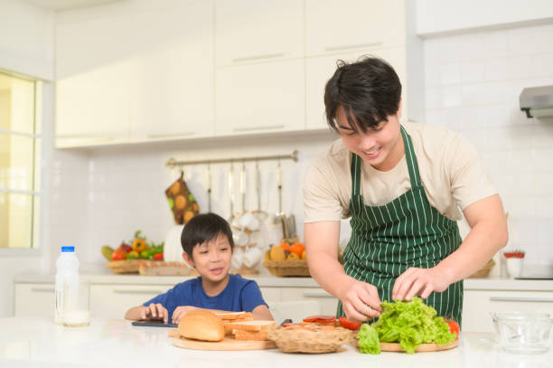 glücklicher junger asiatischer vater, der seinem sohn zu hause in der küche frühstück macht - freedom sandwich bread food stock-fotos und bilder