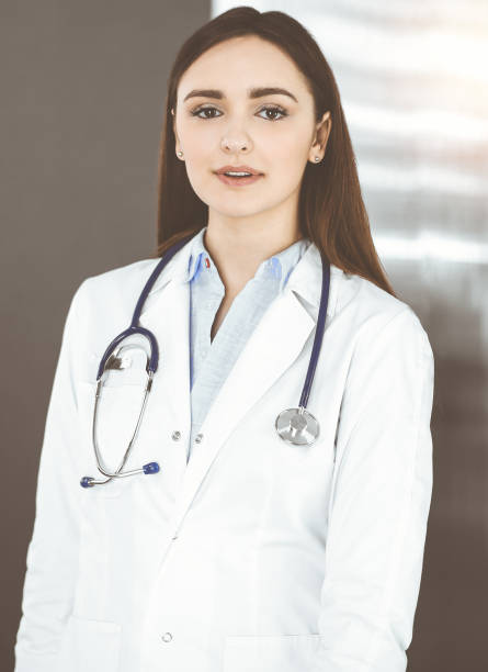 une jeune femme-médecin souriante se tient debout dans une clinique ensoleillée à l’intérieur - portrait doctor paramedic professional occupation photos et images de collection