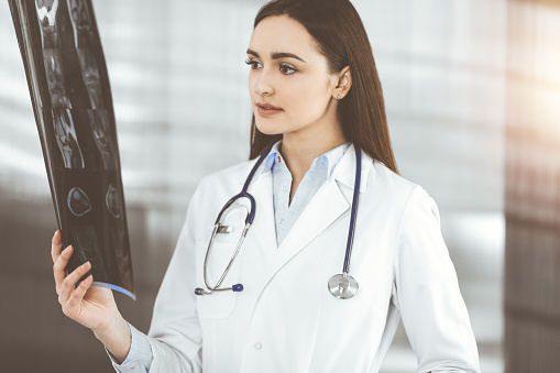 Professional young woman-doctor is looking at her patient's roentgenogram. Physician at work in sunny clinic.