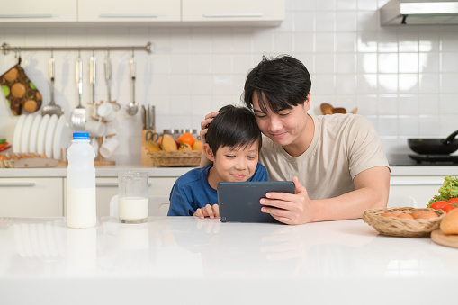 Young Asian father and his son using digital tablet enjoying together in kitchen at home