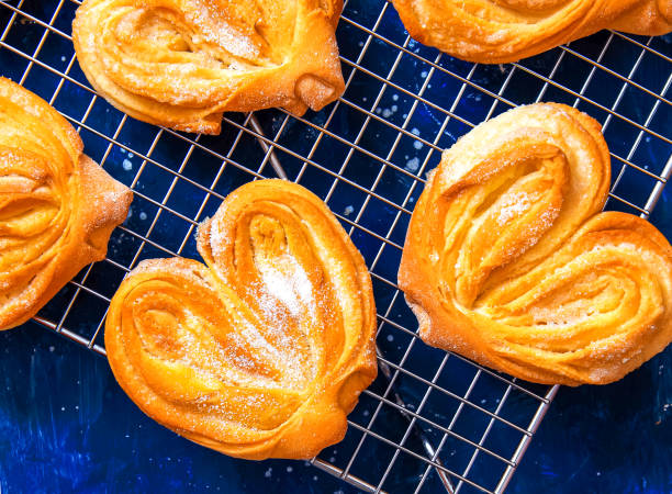 Homemade sugar buns on a cooling rack with sugar for sprinkling. Palmiers, elephant ear, puff pastry cookie Homemade sugar buns on a cooling rack with sugar for sprinkling. Palmiers, elephant ear, puff pastry cookie. plushka stock pictures, royalty-free photos & images