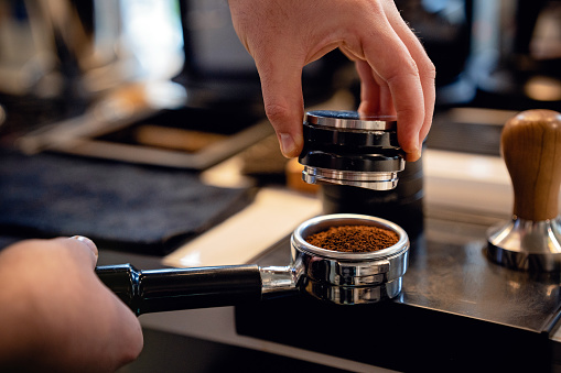 Barista preparing ground coffee with an espresso tamper in a portafilter