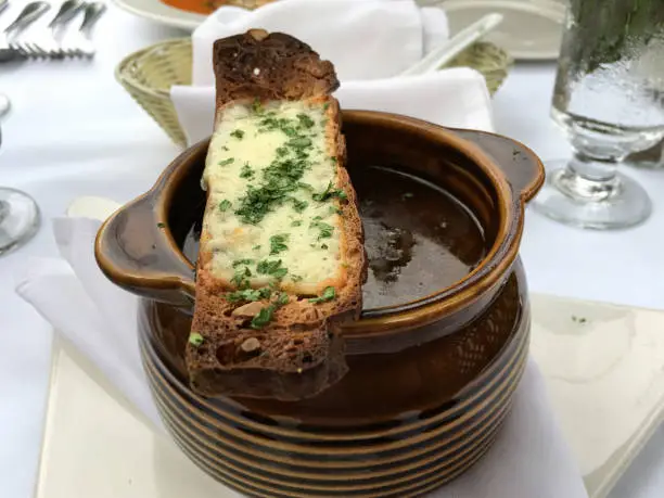Hot crock of French onion soup with a toasted crouton with melted cheese. Delicious bowl of comfort food