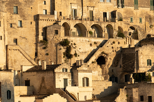 A view of the old buildings of Matera with a cave under the stairs. The old building is at sunset with warm light.