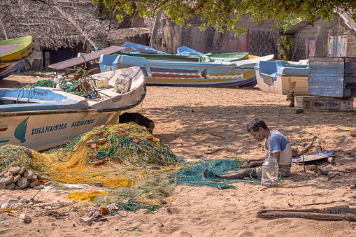 Trincomalee, Eastern Province, Sri Lanka - March 3rd 2023: Fisher man repairing his fishing nets on the popular tropical beach north of the city