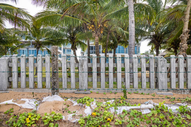 Trincomalee, Eastern Province, Sri Lanka - March 2nd 2023: Concrete fence with barbed wire dividing a hotel garden from the beach. The ground has been reinforced with sandbags of plastic