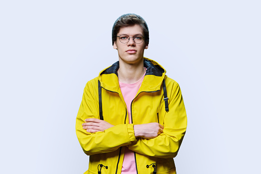 Handsome guy posing in outwear, on white studio background. Trendy young male in knitted hat yellow jacket, looking at camera with arms crossed. Seasonal spring autumn winter clothing, fashion, youth