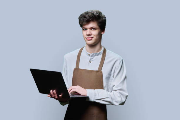 istock Young male in an apron with laptop, on gray studio background 1486345944