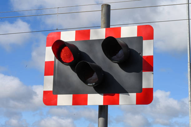 A railway crossing light signal, black three lights with a surround red and white framed boarder, the left hand light lit red