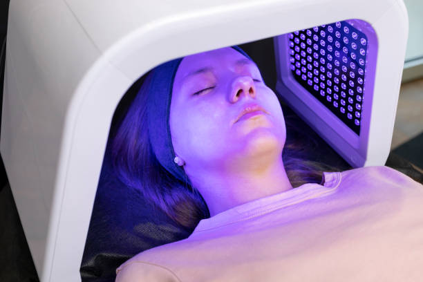 led light mask for face skin therapy, care. Young girl gets problem skin treatment, lying on couch under blue light mask. Stimulation of collagen production, killing acne bacteria. Horizontal máscara de luz led para terapia de la piel facial, cuidado. una niña recibe tratamiento de la piel problemática, acostada en el sofá bajo una máscara de luz azul. estimulación de la producción de colágeno, matando las bacterias del acné. horizonta