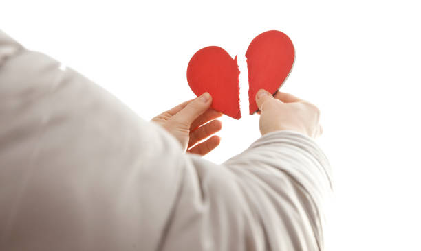The woman is holding two parts of broken heart in her hads in front of the bright sky stock photo