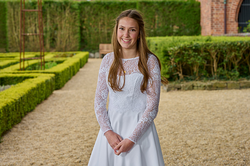 Outdoor portrait of elementary age girl wearing princess dress and paper crown standing in wet garden looking at camera