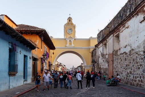antigua, Guatemala – April 05, 2023: Antigua Guatemala 5 april 2023: Cityscape of the main street and yellow Santa Catalina arch with lots of people walking around ruing semana santa