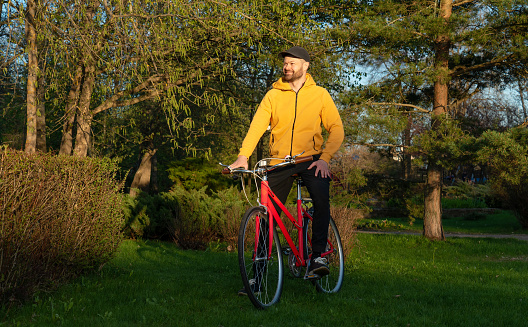 Man in yellow hoodie on a red bicycle in the city park