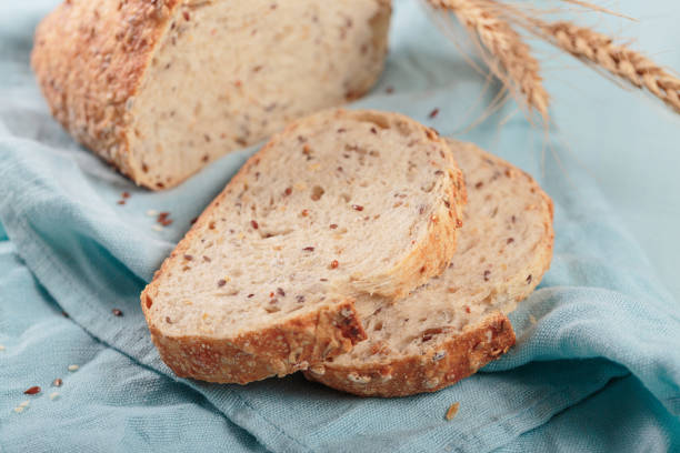 Sliced fresh baked whole grain bread with flax seeds and sesame seeds on light blue board. Bakery products