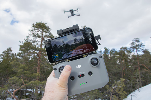 A drone hovering in the air next to a forest scenery