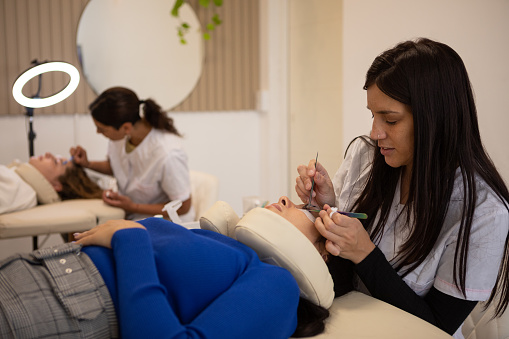 Two argentinean young beauticians applying eyebrow and eyelash beauty treatments as eyebrow lamination and eyelash extension - Buenos Aires - Argentina