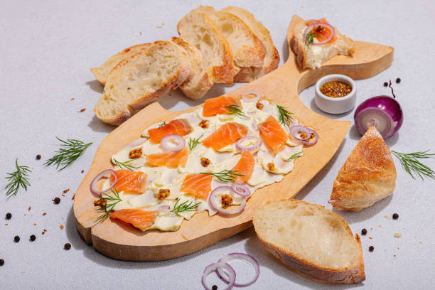 trendiges butterbrett mit lachs, roten zwiebeln, senf und frischem dill. hausgemachter snack mit baguette - dishware butter cutting board agriculture stock-fotos und bilder