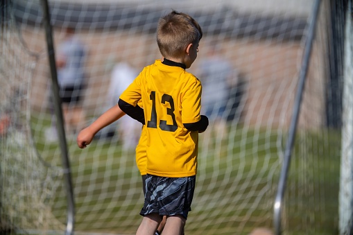 young boy standing on soccer field from behind showing his number 13