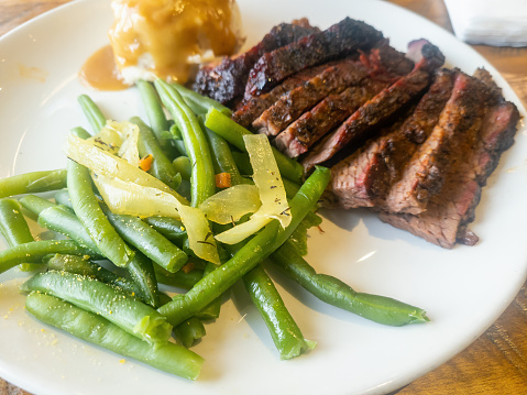 Beef brisket, green beans and mashed potatoes on a white plate on a wood table