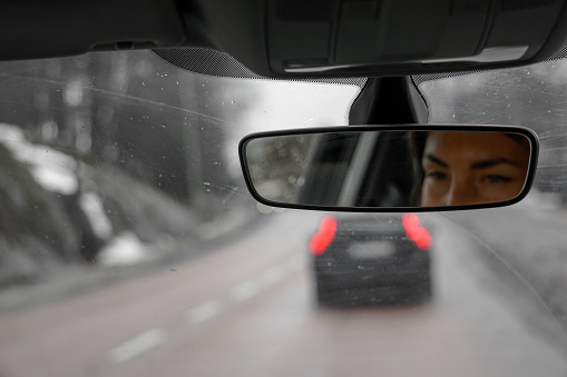 Reflection of a woman in a rear view mirror inside a car