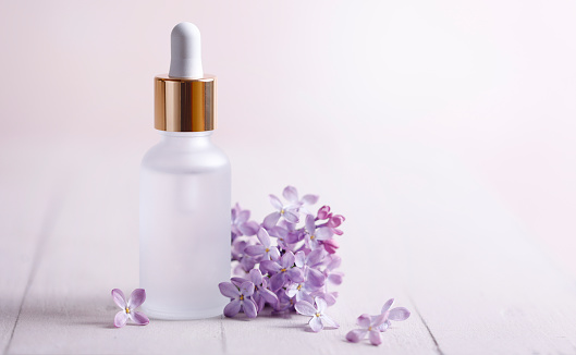 Face serum and lilac flower with copy space