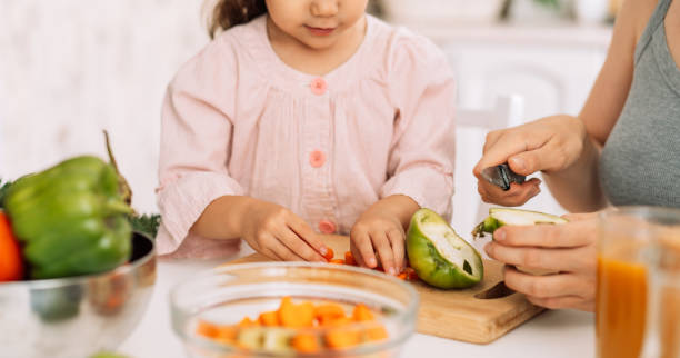 istock Mom and daughter cut vegetables together at the table 1486412498