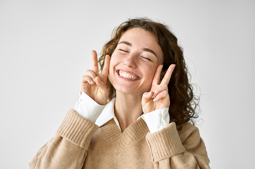 Happy cheerful funny positive playful cute pretty young woman model smiling feeling joyful showing victory peace hand gestures laughing posing having fun isolated on white background.