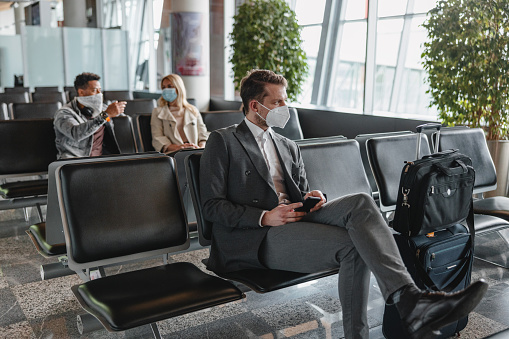 A Caucasian businessman in a grey suit wearing a face protective mask at the airport business lounge.