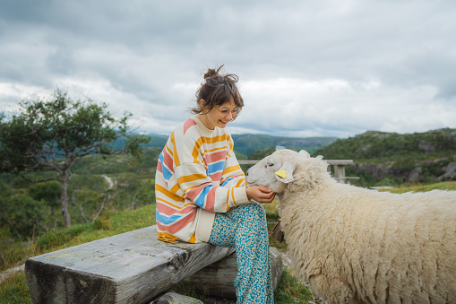 Young Caucasian woman petting a sheep in Norwegian countryside