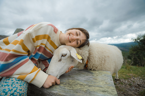 Young Caucasian woman petting a sheep in Norwegian countryside