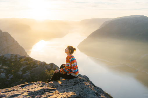 Young Caucasian woman sitting on Preikestolen and looking at view