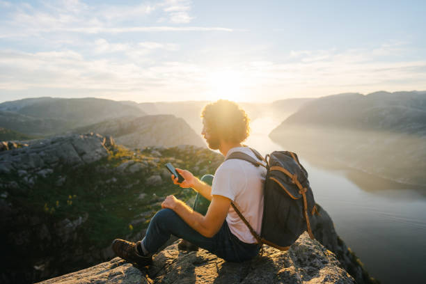 istock Man sitting on Preikestolen and using smartphone 1486451131