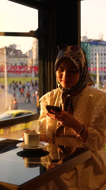 young muslim woman sitting near the window of a  cafe