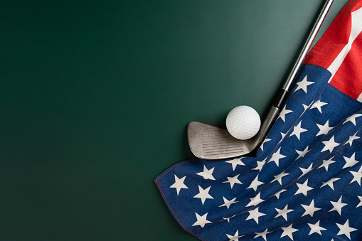 Golf ball and golf club with flag of USA on green table background, sport concept