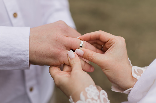 groom puts a gold wedding ring on the bride's finger