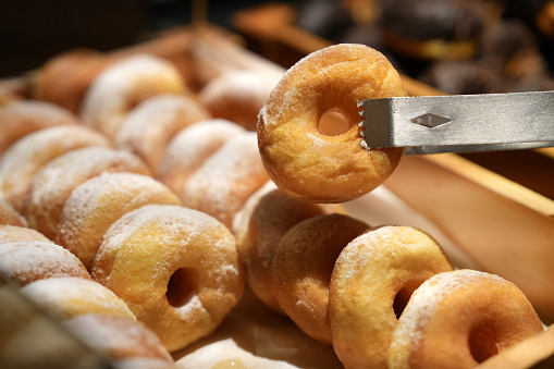 Cropped image of a woman at the buffet bar picking up a sugar doughnut with serving tongs.