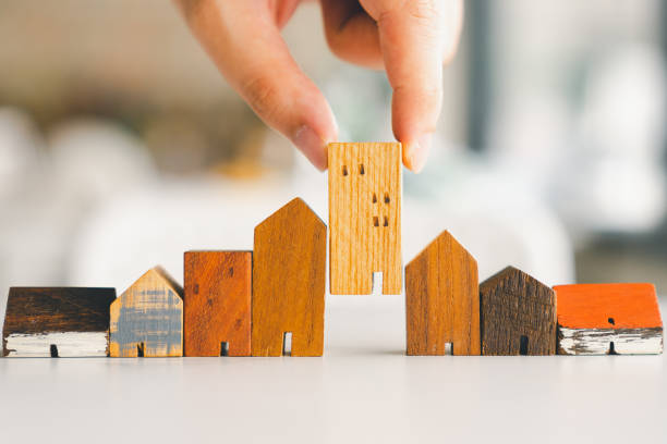 Hand choosing mini wood house model from model and row of coin money on wood table, selective focus, Planning to buy property. Choose what's the best. A symbol for construction ,ecology, loan concepts stock photo