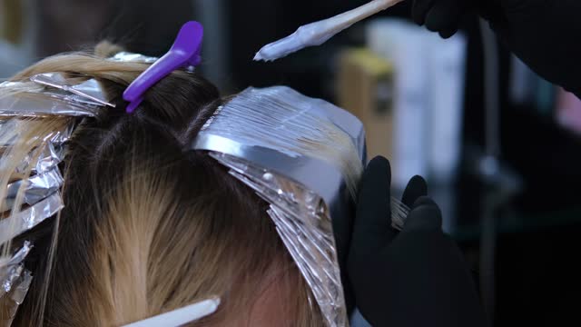 Coloring dark roots white in a beauty salon. The hairdresser highlights the hair and wraps it in foil.