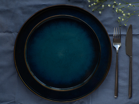 Festive table setting with flowers on blue background, flat lay. Celebration. Dark serving composition. Elegance blue tablescapes. View from above.