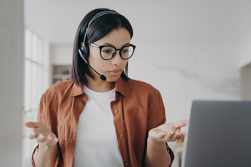 Young european woman has online conference. Businesswoman in headset and glasses is talking. Manager or business assistant is sitting at the desk and having interview. Confident girl at workplace.