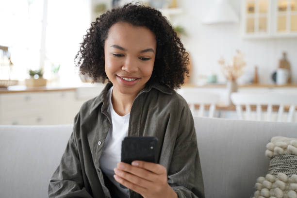 istock Young biracial girl chat or post at social network, using smartphone apps, sitting on sofa at home 1486502719