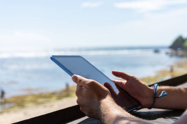 istock Man hands with tablet on blurred summer beach background 1486508006