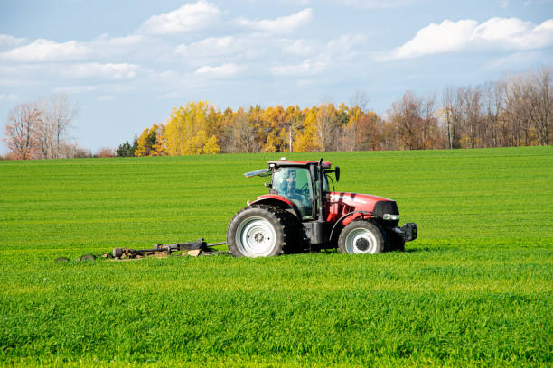 Close-up larger farm tractor with rotary cutter trailer on farmland meadow field, colorful fall foliage, cloud blue sky South Lockport, Niagara County, Upstate New York, USA. Agriculture industrial primer plano de tractor agrícola más grande con remolque cortador rotativo en el campo de praderas de tierras de cultivo, colorido follaje de otoño, cielo azul nube south lockport, condado de niágara, norte del estado de nueva york, ee. uu.