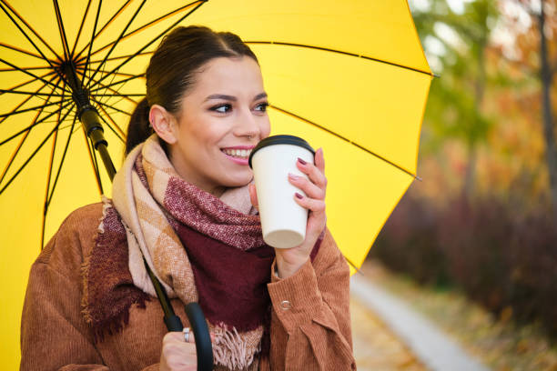 Caucasian woman with coffee and yellow umbrella smiling in autumn. stock photo