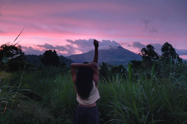 Rear shot of unrecognizable woman  stretching her arms upright while watching a beautiful sunrise over a mountain.